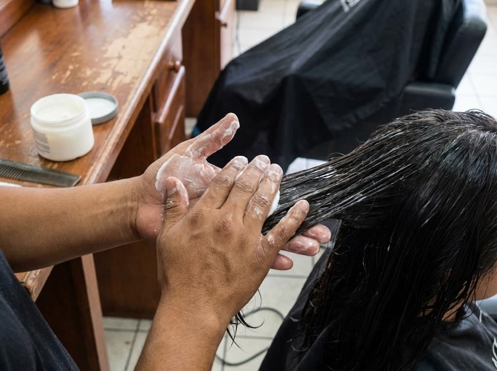 Manos de estilista aplicando tratamiento capilar cremoso al cabello de clienta